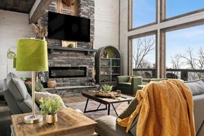 Ein modernes Wohnzimmer mit Kamin aus Stein, einem Flachbildfernseher und einem großen Fenster mit Blick ins Freie.