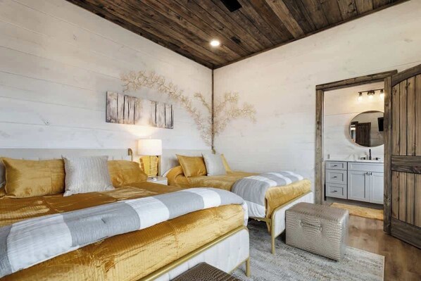 Un dormitorio con dos camas, techo de madera, un espejo y un baño visible a través de una puerta abierta.