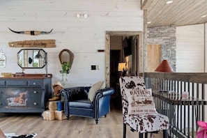 Un interior rústico con un sofá de cuero, una silla estampada con motivos de vaca, un aparador de madera y una pared de piedra.
