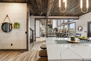 A modern kitchen with a large island, wooden ceiling, and large windows.