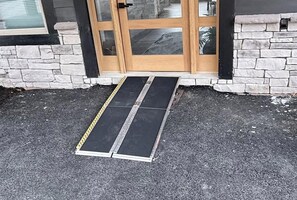 A set of wooden double doors with glass panels, a stone wall, and a black ramp leading to the entrance. - 7-Bedroom Luxury Cabin with Indoor Pool, Rooftop & Pickleball Court (Sevierville)