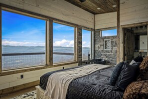 A bedroom with a large bed, a stone fireplace, and a view of mountains through large windows.