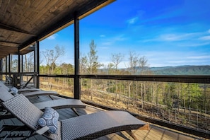 Un espacio de estar al aire libre techado con sillones reclinables y vistas a un paisaje montañoso.