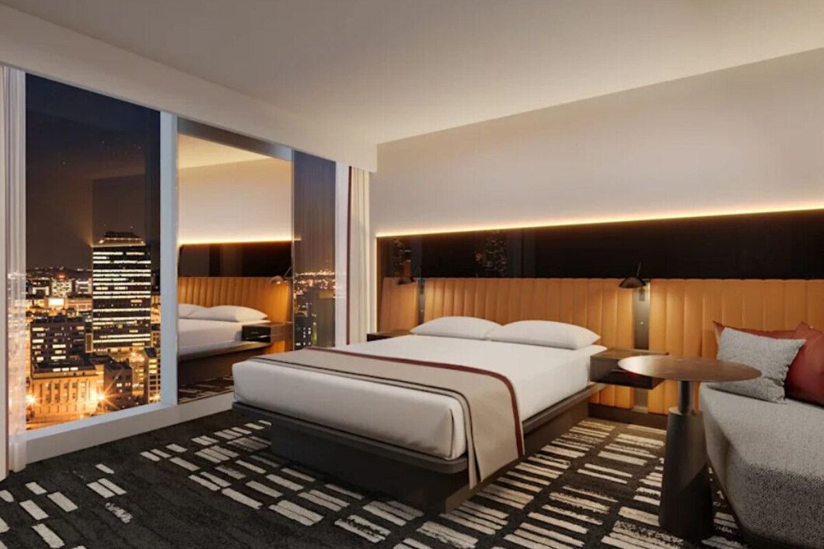 A hotel room with a bed, a seating area, a view of the cityscape, and a large window.