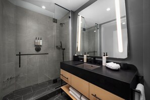 A modern bathroom with a glass shower enclosure, a black countertop, and a large mirror. - Signia Hilton Indianapolis (Indianapolis)
