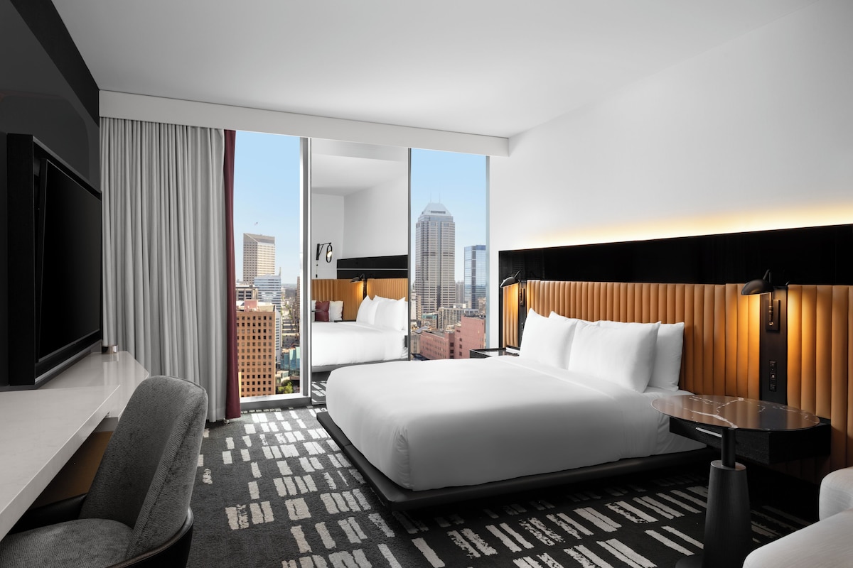 A modern hotel room with a large bed, a desk, a chair, and a city view.