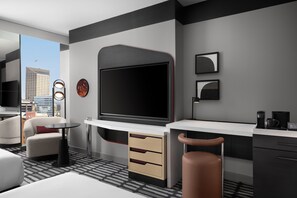 A modern hotel room with a large flat-screen TV, a desk, a chair, a sofa, and a view of the cityscape. - Signia Hilton Indianapolis (Indianapolis)