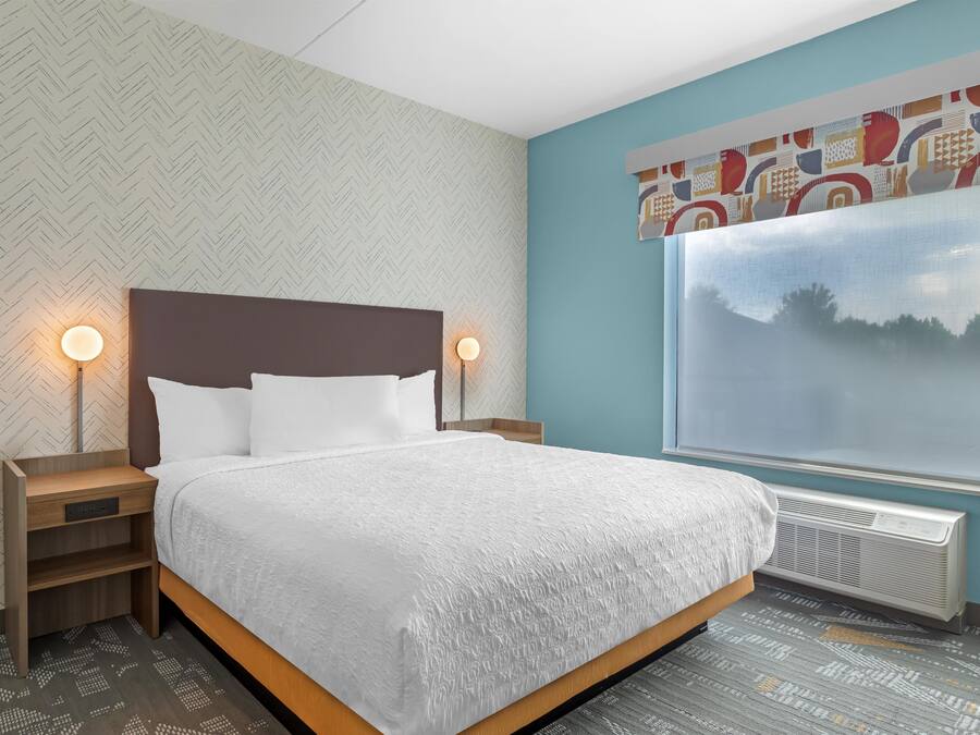 A hotel room with a bed, nightstands, a window with a view, and patterned wallpaper.