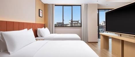 A hotel room with two beds, a large window with a city view, a flat-screen TV, and a wooden desk.
