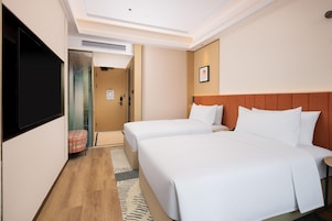 Habitación de hotel con dos camas, televisión de pantalla plana, cabecero de madera y una pequeña zona de estar.