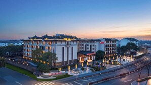 A multi-story hotel with traditional and modern architectural styles, a landscaped courtyard, and a well-maintained road. - Hilton Garden Inn Tongxiang Wuzhen (Jiaxing)