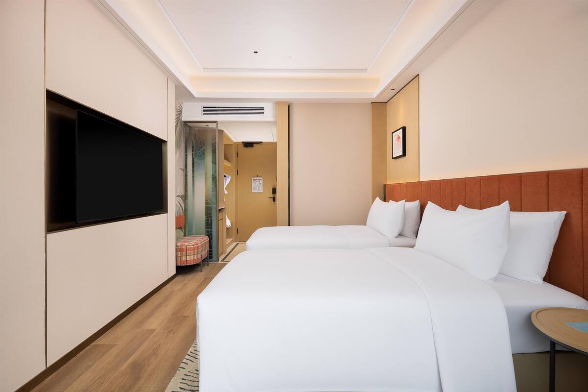 Ein Hotelzimmer mit zwei Betten, einem Fernseher, einem kleinen Tisch und einer Tür zu einem Badezimmer.