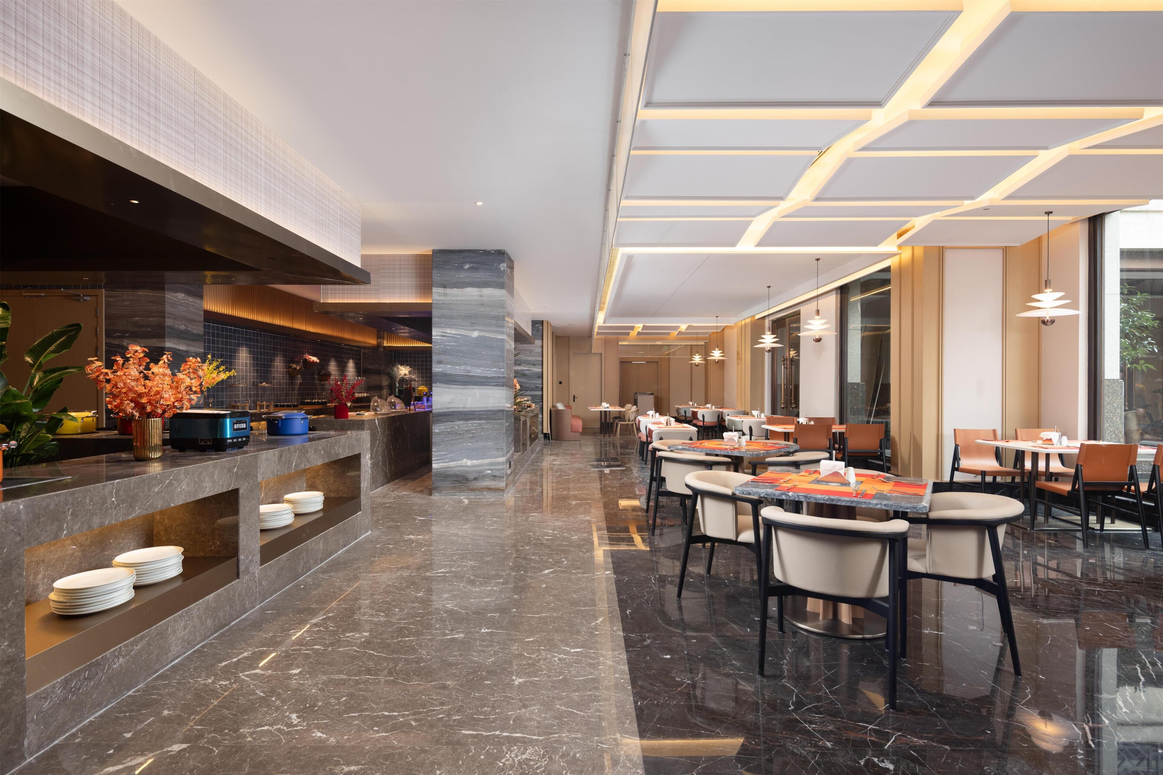 Un moderno vestíbulo de hotel con piso de mármol, una mesa de recepción y un área de comedor con mesas y sillas.