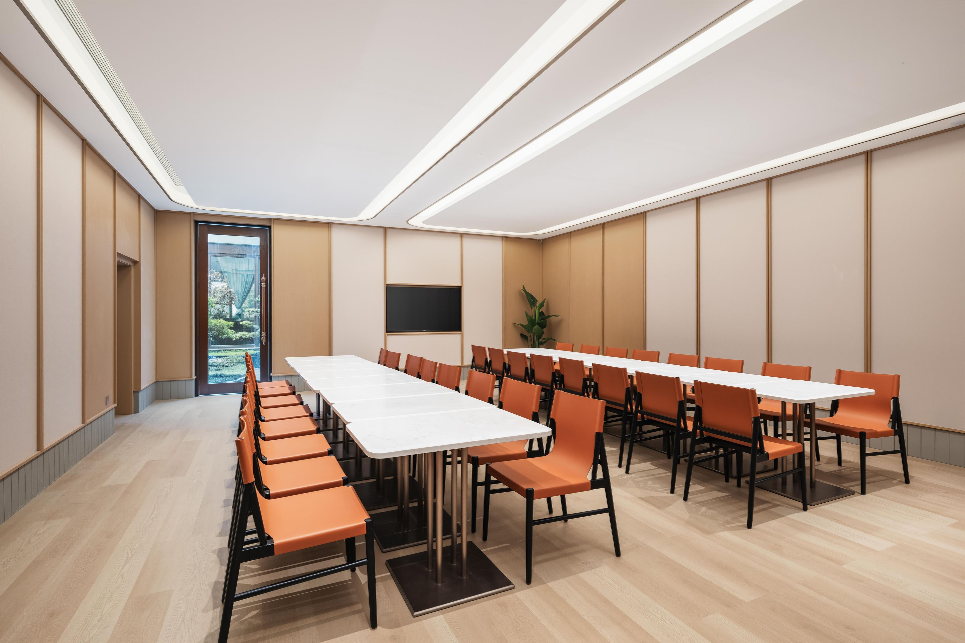 Ein Konferenzraum mit einem langen Tisch, mehreren Stühlen, einer Tafel und einer Pflanze.