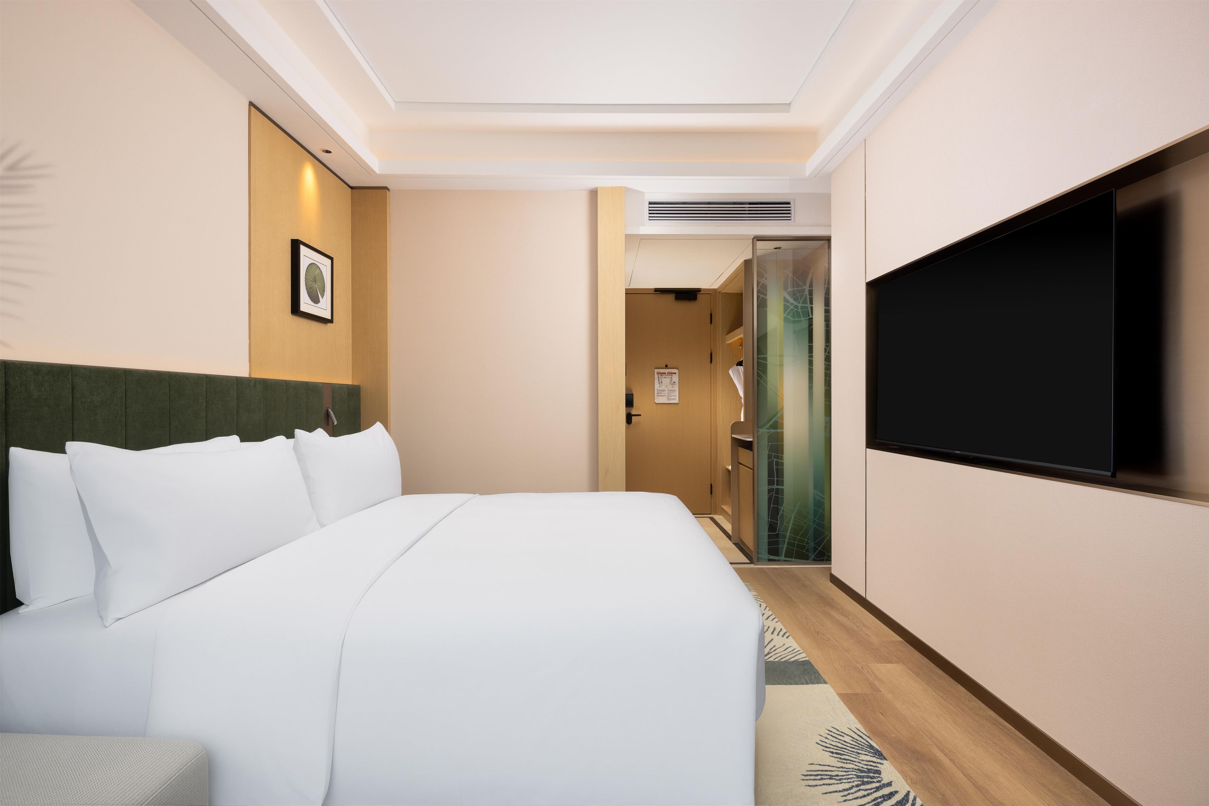 A hotel room with a bed, a television, a door, and a wall-mounted picture.