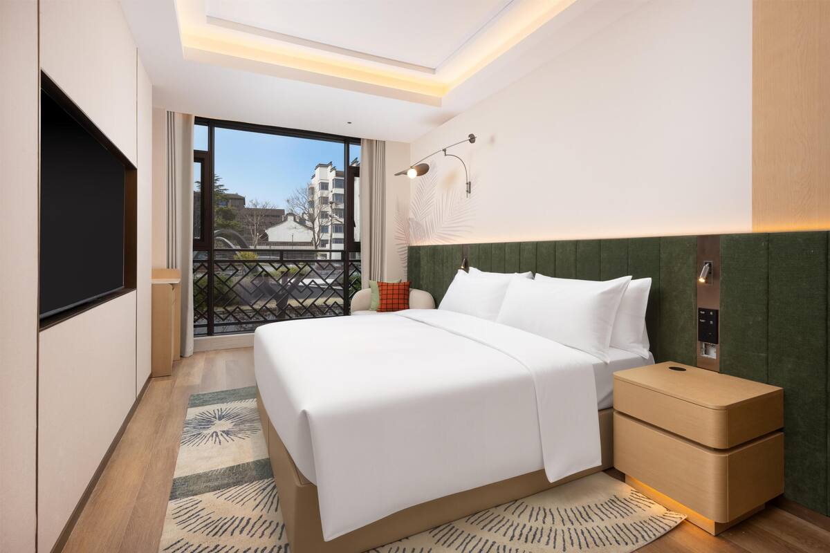Ein Hotelzimmer mit Bett, Nachttisch, Fernseher, einem Balkon mit Blick und einer modernen Leuchte.