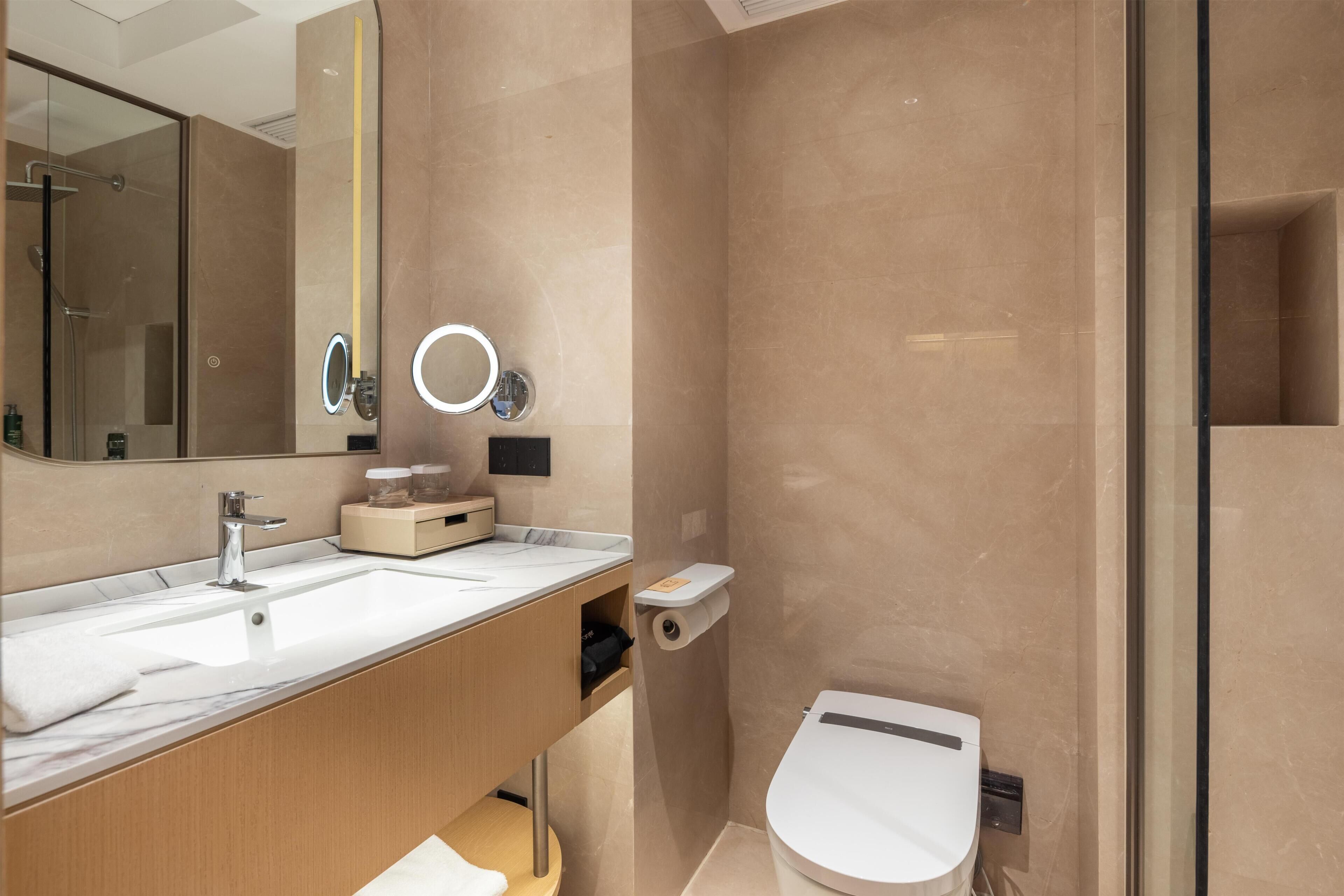 A modern bathroom with a large mirror, a sink, a toilet, and a shower area.