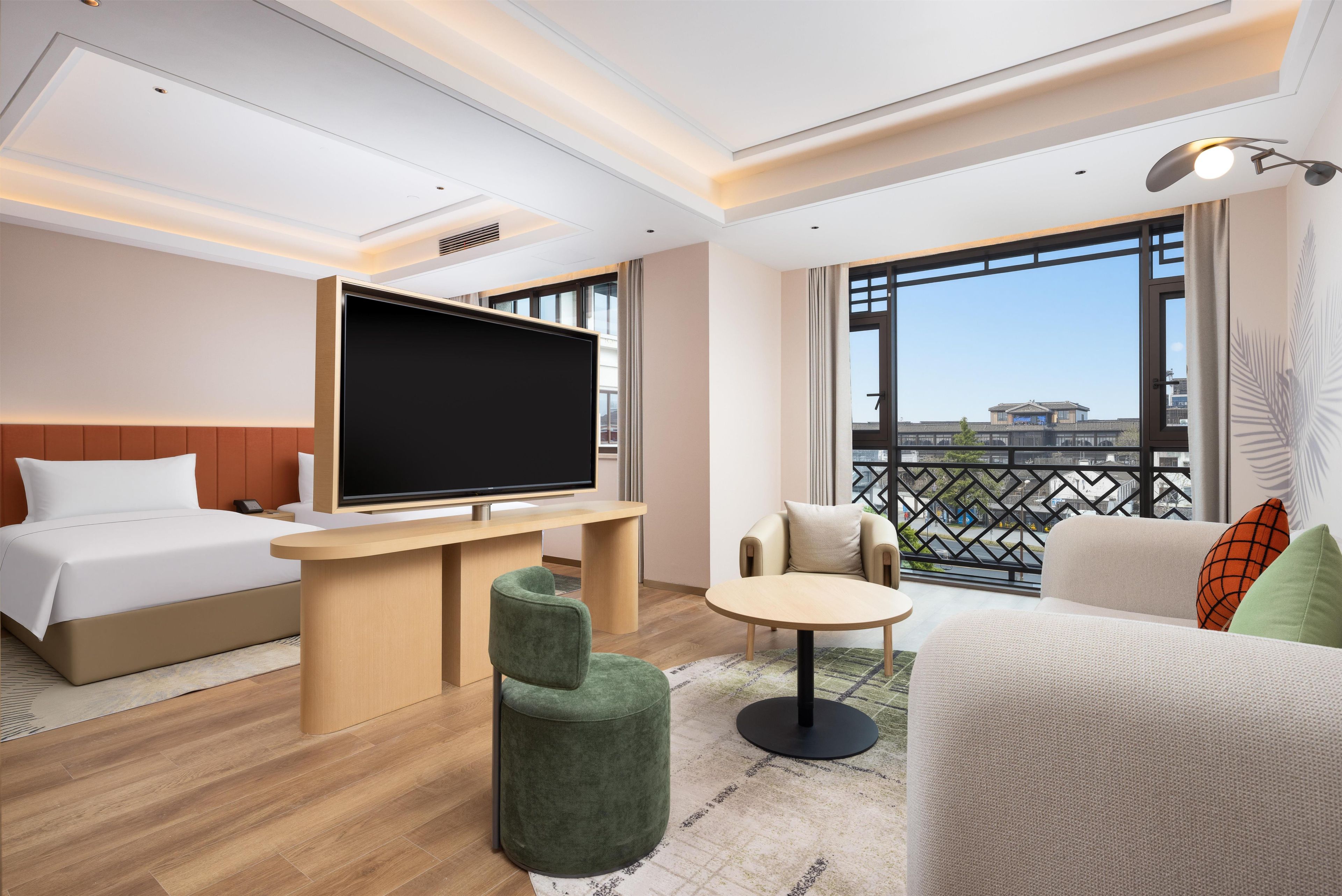 Ein Hotelzimmer mit Bett, Fernseher, kleinem Tisch, zwei Stühlen und einem Balkon mit Aussicht.