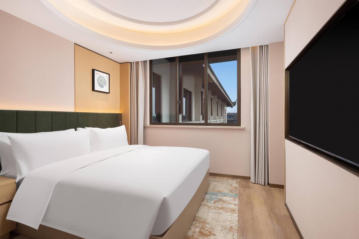 Ein Hotelzimmer mit Bett, Nachttisch, großem Fenster und Flachbildfernseher.