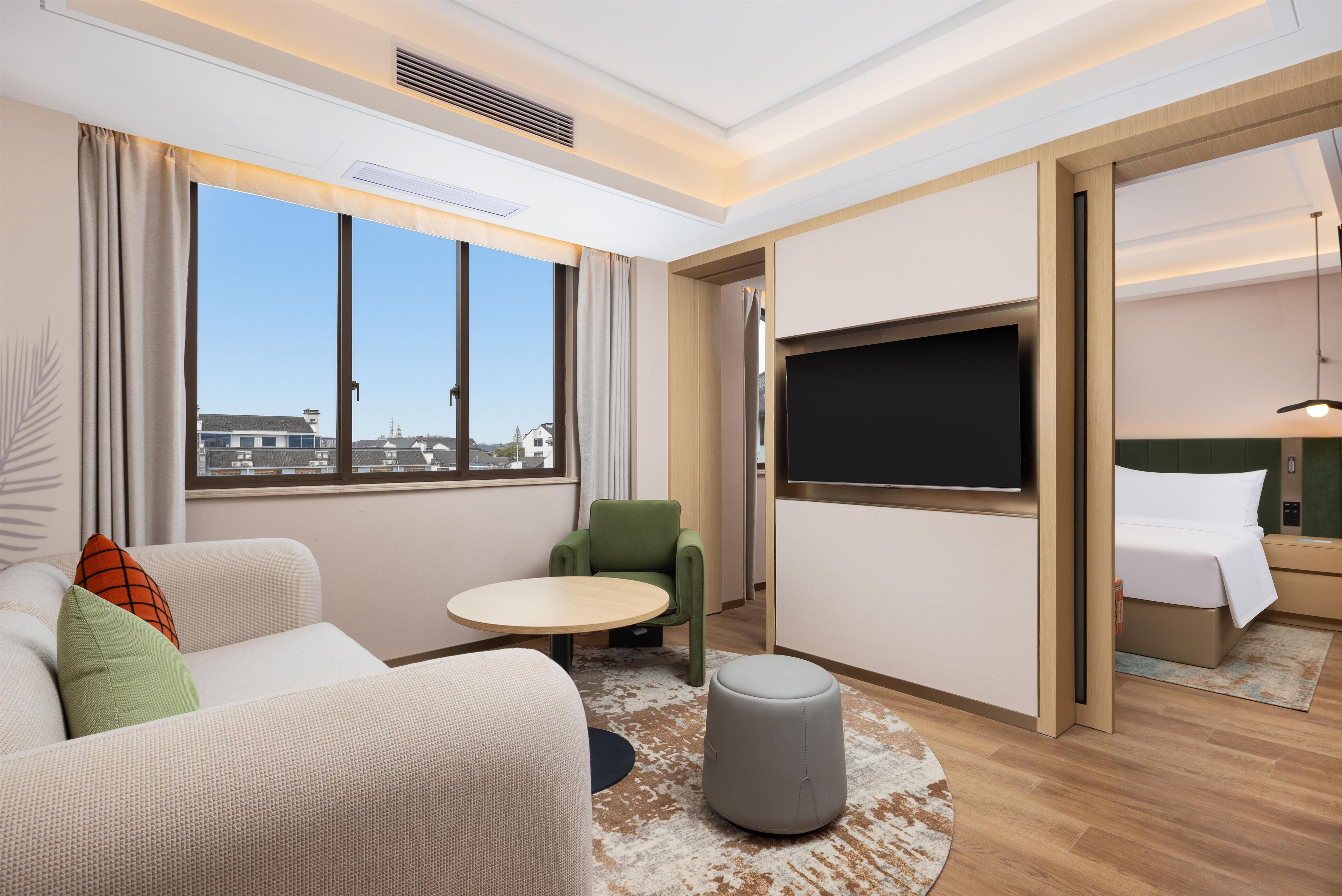 Una habitación de hotel con un sofá, un sillón verde, una mesa redonda, un televisor y una cama.
