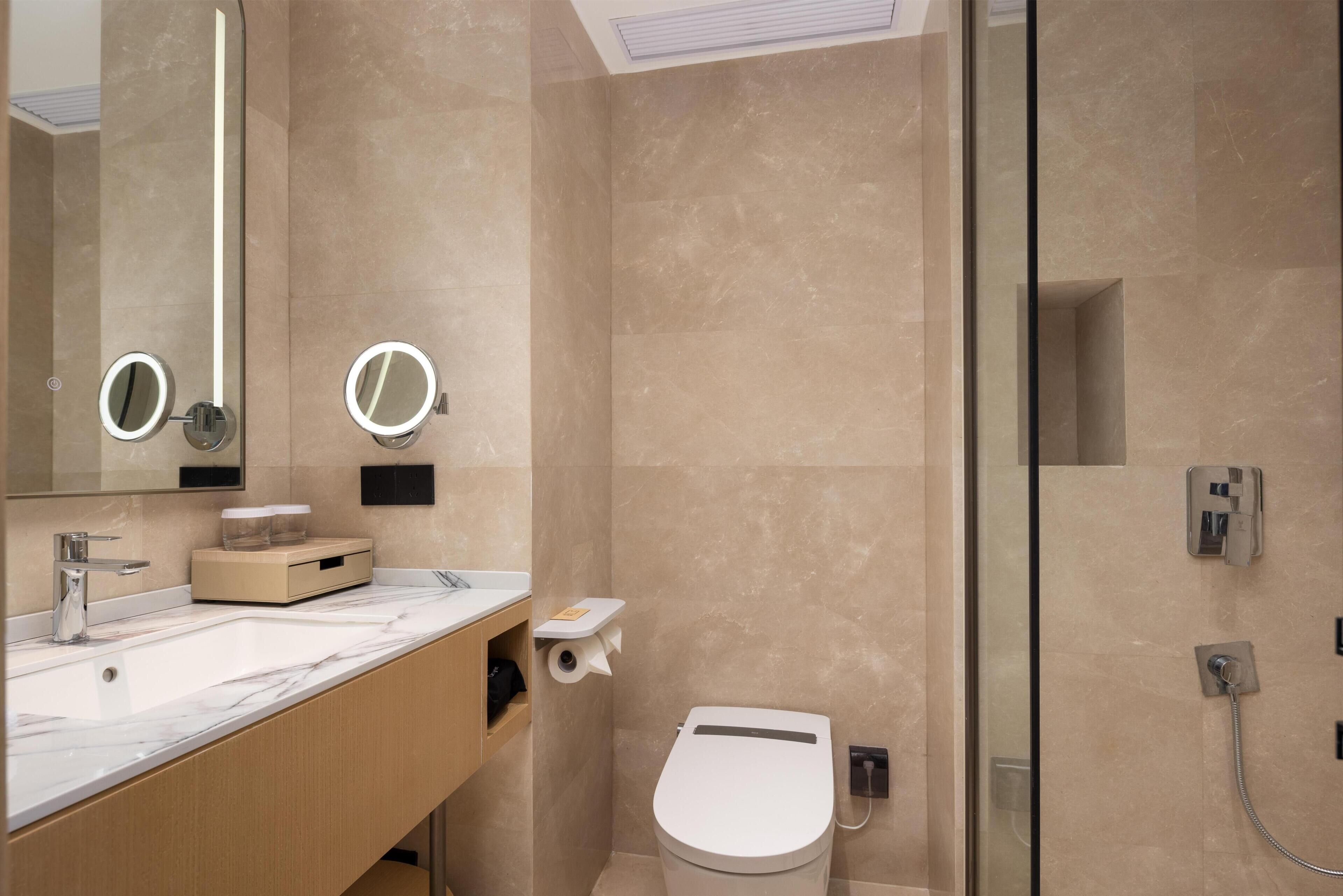 A modern bathroom with a marble sink, two round mirrors, a toilet, and a glass-enclosed shower.