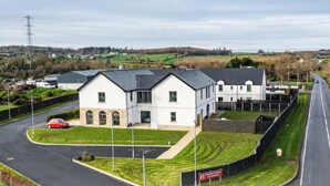 A large, white building with a grey roof, surrounded by a well-maintained lawn and a curved road. - Homestead Hillsborough, Triple Deluxe Suite (Hillsborough)