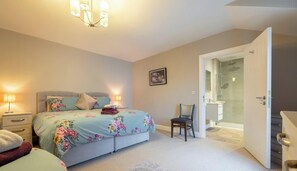 Un dormitorio con cama, lámparas de noche, una silla, una puerta que da a un baño y un candelabro.