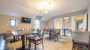 A dining area with a long table, multiple chairs, a television mounted on the wall, and a chandelier. - Homestead Hillsborough, Triple Deluxe Suite (Hillsborough)