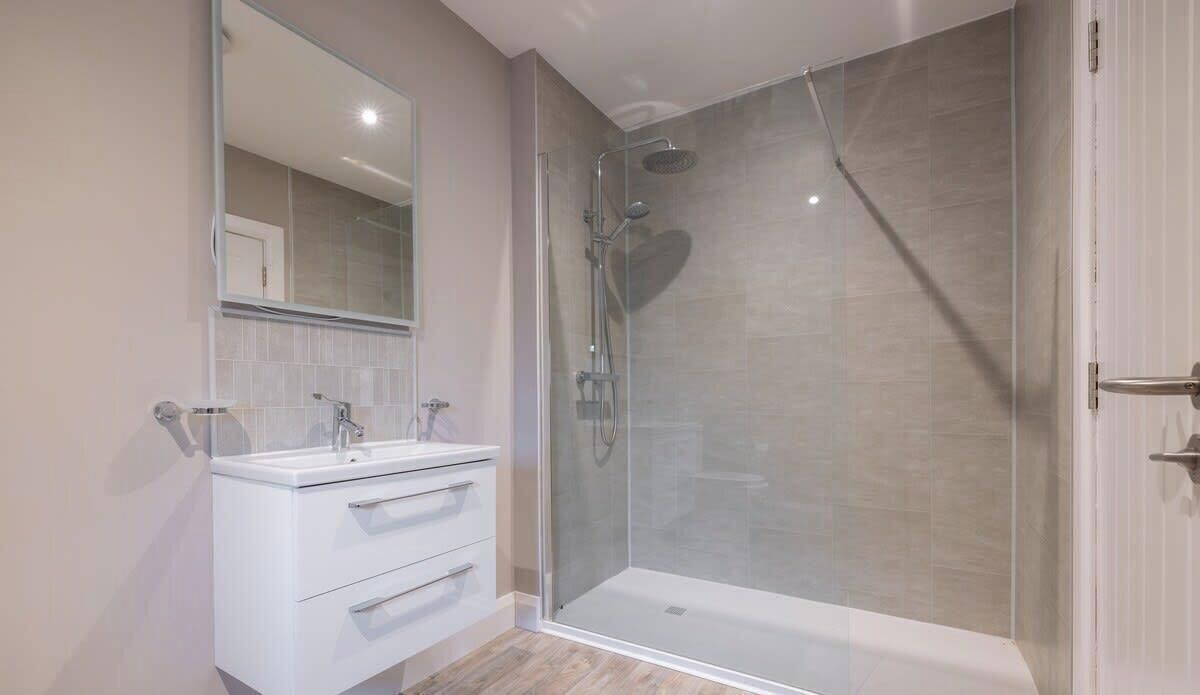 A modern bathroom with a glass-enclosed shower, a white vanity with a mirror, and a door to the right.