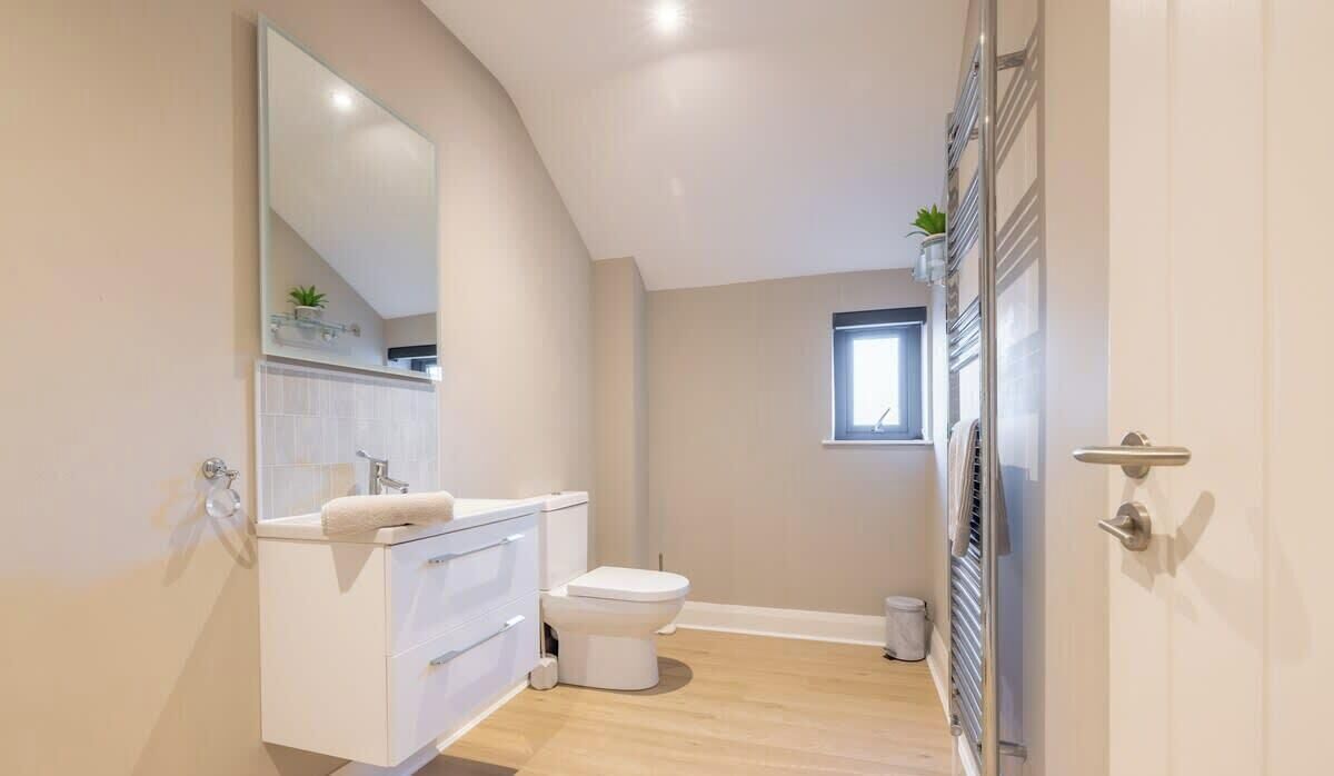 Ein modernes Badezimmer mit einem weißen Waschtisch, einer Toilette, einem Spiegel und einem kleinen Fenster.