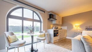 A modern kitchen with a large window, a dining area with two chairs, a sofa, and a small table.