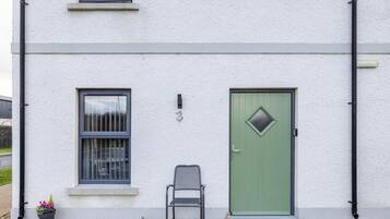 A two-story building with a green door, a window with a metal grill, and a chair outside.