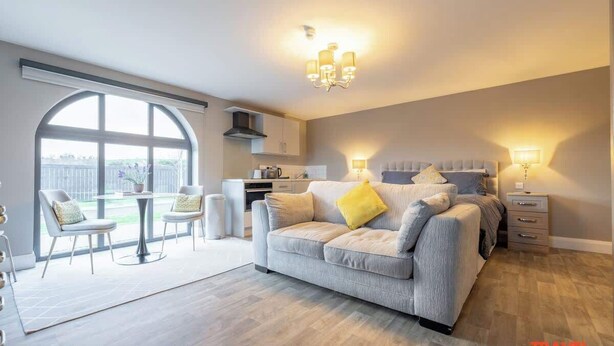 A modern hotel room with a large window, a dining area, a sofa, and a bed.