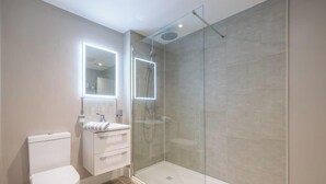 A modern bathroom with a glass-enclosed shower, a white toilet, and a vanity with a mirror.