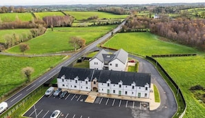 A building with a parking lot, a road, and green fields in the background.