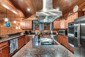 A modern kitchen with wooden cabinets, stainless steel appliances, and a granite countertop. - Gatlinburg 7BR | Theater + 2 Game Rooms (Gatlinburg)