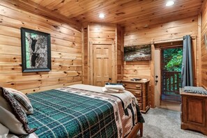 Ein Schlafzimmer einer Holzhütte mit einem Bett, einer Kommode, einem gerahmten Bild an der Wand und einer Tür, die auf einen Balkon führt.