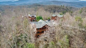 Un chalet composé de plusieurs bâtiments, entouré de forêts et de montagnes.