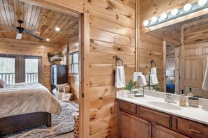Ein Holzhütten-Innenraum mit einem Bett, einem Badezimmer mit Spiegel und einem Deckenventilator.