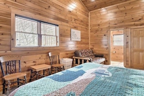 A cozy cabin room with a bed, a chair, a table, and a window with blinds. - 7-Bedroom Gatlinburg Cabin with Theater, Two Game Rooms & Hot Tub (Gatlinburg)