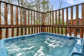 Ein Whirlpool auf einer Holzterrasse mit Blick auf Bäume und ein Gebäude im Hintergrund.