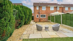A residential backyard with a patio, two wicker chairs, a small table, a brick house, and a green fence. - 2 Bed home, close to the hospital and town centre - Pass the Keys (Shrewsbury)