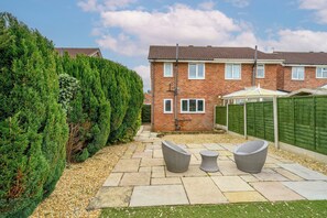 A residential backyard with a patio, two wicker chairs, a small table, a brick house, and a green fence. - 2 Bed home, close to the hospital and town centre - Pass the Keys (Shrewsbury)