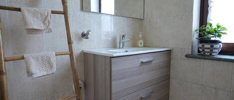 Een badkamer met een houten ladder, een spiegel, een wastafel met een zeepdispenser en een plant in een pot op de vensterbank.