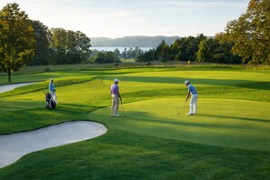 Een golfbaan met zandbunkers, bomen en een meer op de achtergrond.