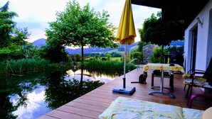 A wooden deck with a table and chairs, a hammock, and a cat sitting on the deck. - Room-charming Guest Room in Ebbs Nature (Ebbs)