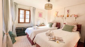 A hotel room with two beds, a window with curtains, a bedside table with a lamp, and a shelf with decorative items. - La Fetta Di Cima, Porlezza, Italy (Porlezza)