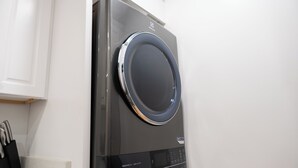 En modern, kompakt tvätt- och torkmaskin med en kontrollpanel och en rund lucka, installerad i ett kök med vita köksluckor.
