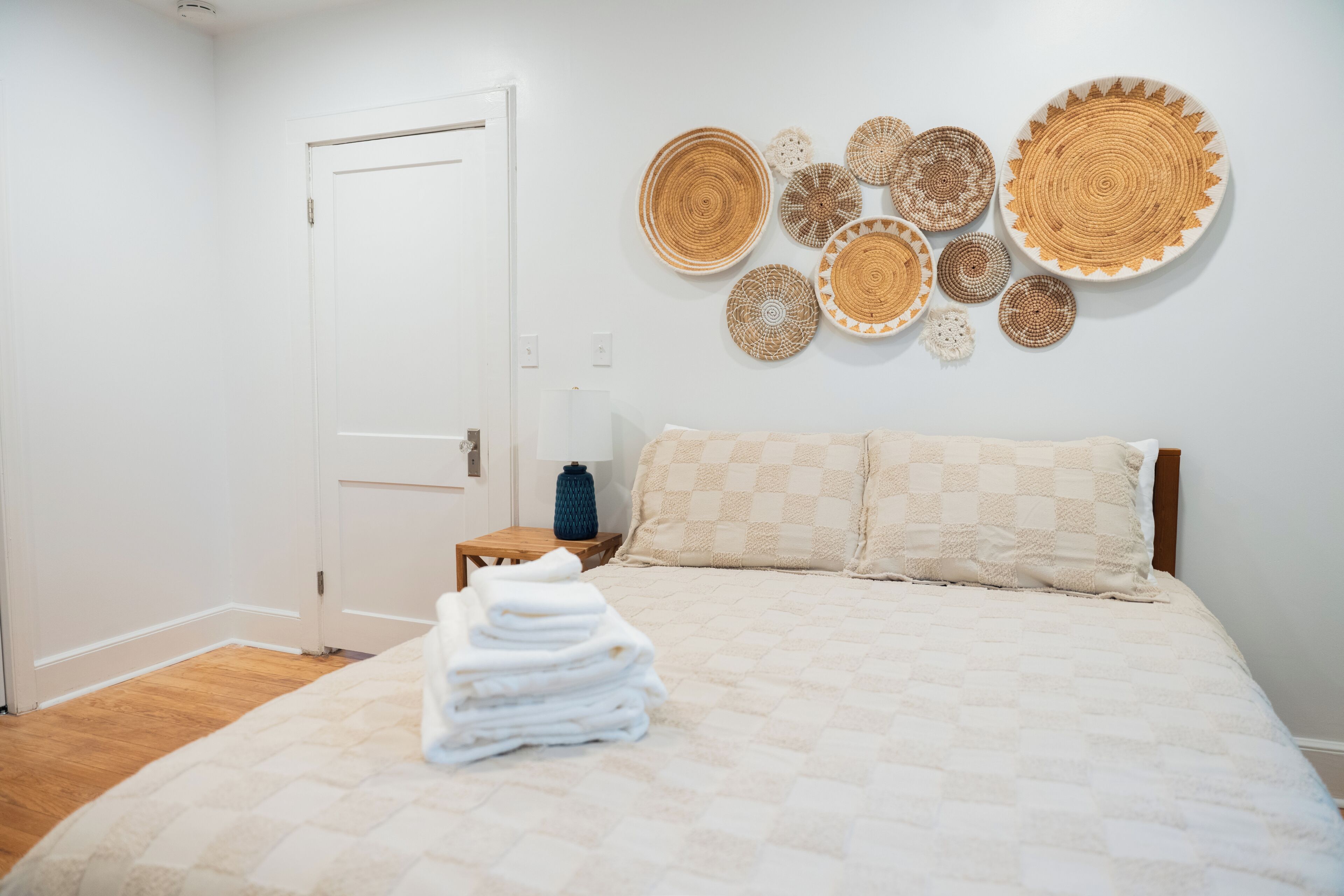 A bedroom with a bed, a stack of towels, a nightstand, a lamp, and wall decor.