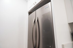 Un refrigerador de acero inoxidable con la etiqueta 'FRIGIDAIRE', armarios blancos y una pequeña repisa sobre la puerta.